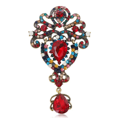 Front view of the ornate crystal dangle brooch showing an ornate scrollwork brooch with clustered stones and a teardrop 