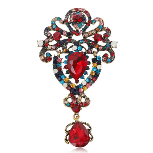 Front view of the ornate crystal dangle brooch showing an ornate scrollwork brooch with clustered stones and a teardrop 
