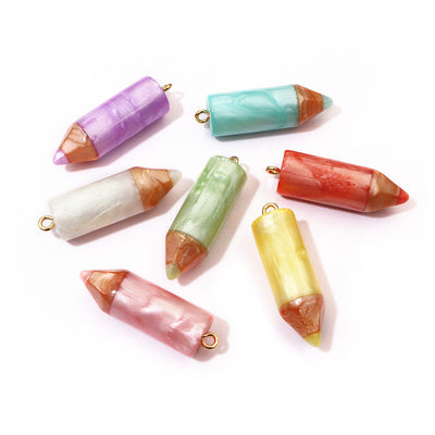Front overview of pastel crayon shaped resin charms with gold tone loops arranged on a light background