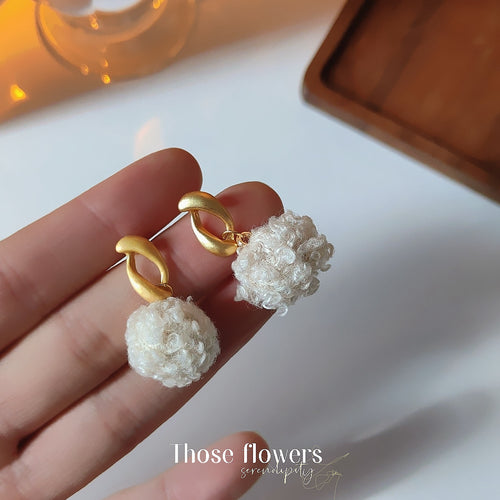 Cream yarn pom gold loop earrings on brown wood tray