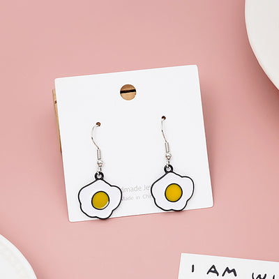 Fried egg enamel earrings on white jewelry card against pink background