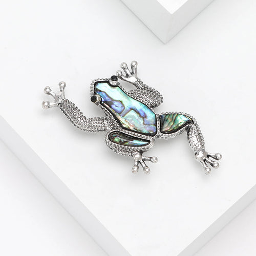 Silver frog brooch angled on white geometric blocks