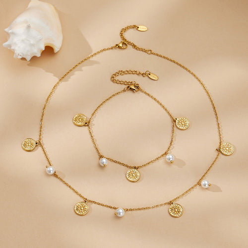 Gold sun disc and pearl necklace with matching anklet beside white shell