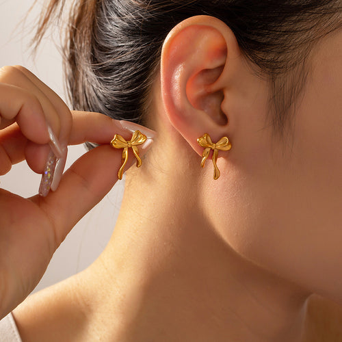 Gold bow stud earrings worn and held beside ear