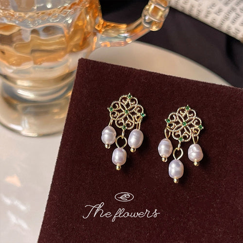 Filigree pearl earrings on dark red pad near glass mug