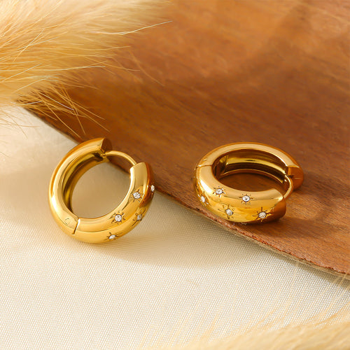 Pair of gold star rhinestone huggie hoops on wood surface