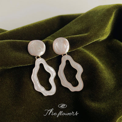 Cream irregular hollow drop earrings on green velvet fabric