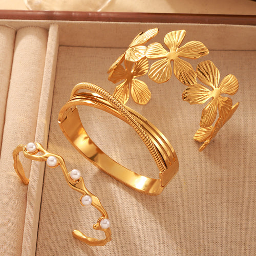 Three gold open cuffs flower pearl wave and triple band on beige tray
