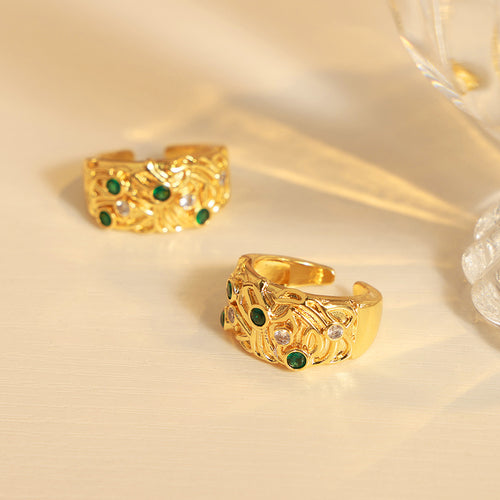 Two gold embossed open rings with green stones on light surface