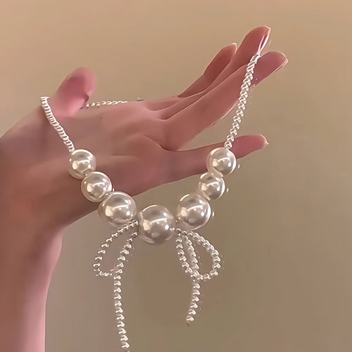 white pearl look bow fringe collar necklace with metal tone details shown in an on-ear styling view
