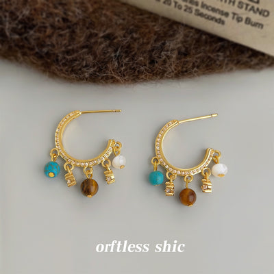 Pair of gold pavé C-hoop charm earrings on gray surface with wool