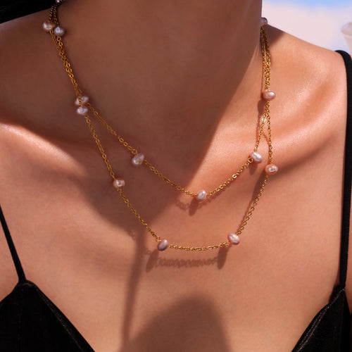 Model wearing layered gold station necklaces with pink and purple freshwater pearls