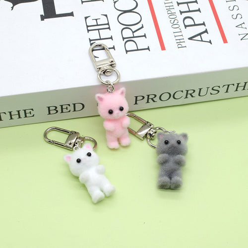 White pink and gray flocked cat keychains scattered on green surface near book