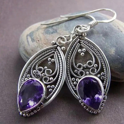 Pair of silver openwork teardrop purple stone earrings on a stone