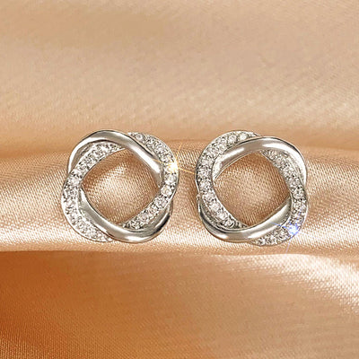 Pair silver intertwined CZ knot stud earrings on satin fabric