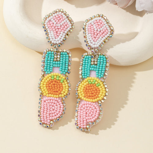 Pink, teal and yellow beaded HOP earrings shown close up on a cream dish