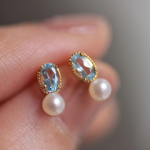 Pair of blue oval pearl studs on fingertips soft focus