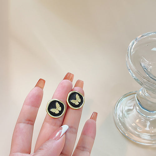 Gold rim black butterfly studs held between fingers