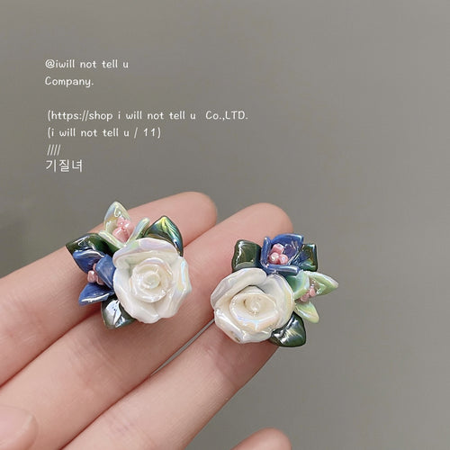 White ceramic rose blue leaf floral studs held between fingers