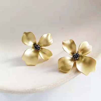 Gold matte four-petal flower stud earrings on cream surface