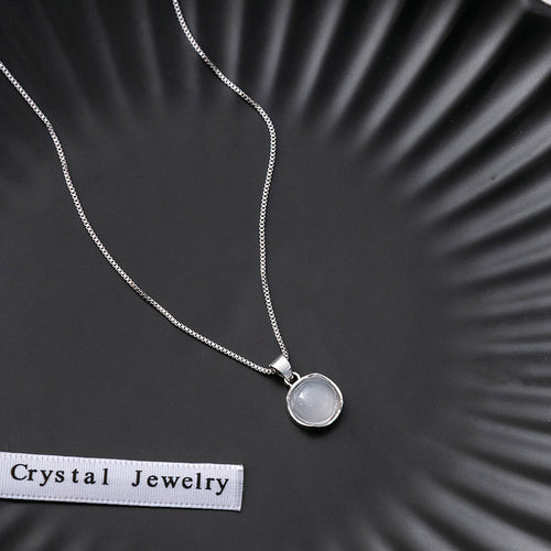 Close-up of milky white cabochon pendant on silver box chain with Crystal Jewelry ribbon