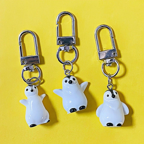 Three white resin penguin keychains with silver lobster clasps on yellow background