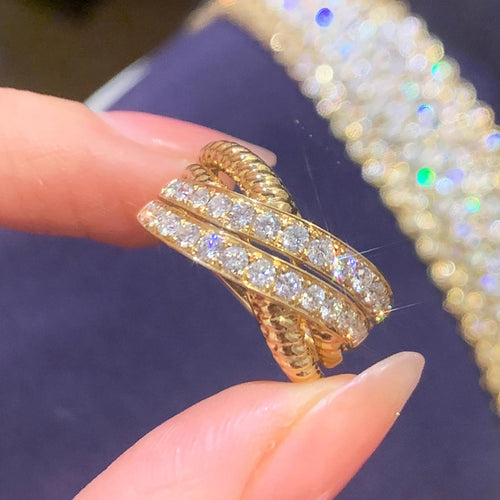 Gold cross over pave ring held between fingers close-up