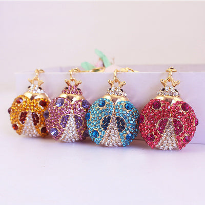 Four rhinestone ladybug keychains in gold, purple, blue, and pink.