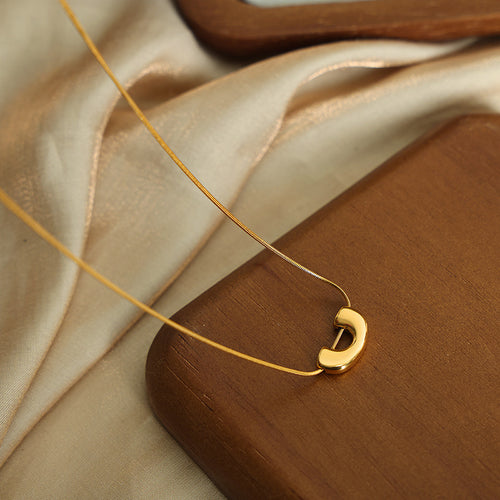 Gold U-lock snake necklace on wood tray and satin