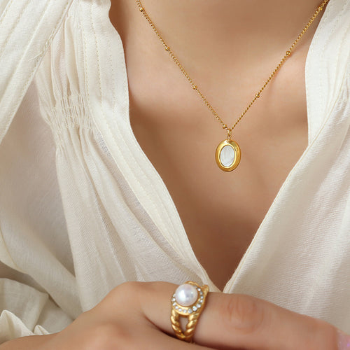 Gold oval mother-of-pearl pendant necklace on cream blouse