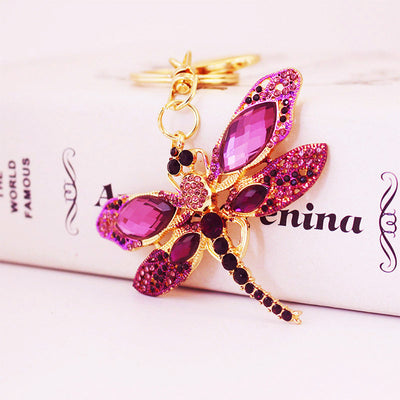 Angled front view of a pink and purple stone dragonfly charm on gold-tone keychain hardware.