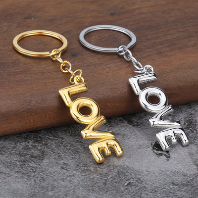 Gold-tone and silver-tone LOVE keychains rest side by side on a wood surface.