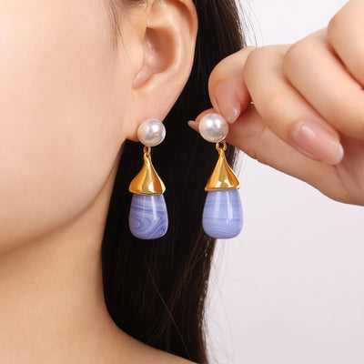 Model holding blue resin gold-tone pearl drop earrings near ear