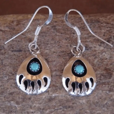 Antique silver bear paw turquoise dangle earrings on stone surface