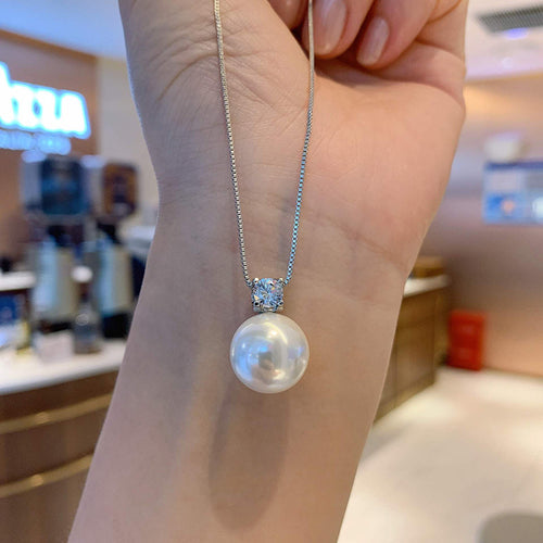 Silver faux pearl clear pendant necklace held against hand in store light