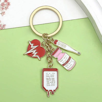 Gold-tone keyring displayed on a green background with red heart, thermometer, vial and IV bag charms.