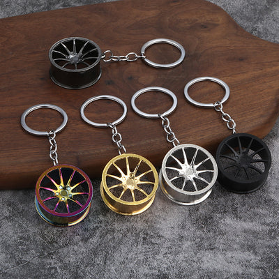 Five wheel rim keychains shown in rainbow, gold, silver, gunmetal, and matte black finishes.