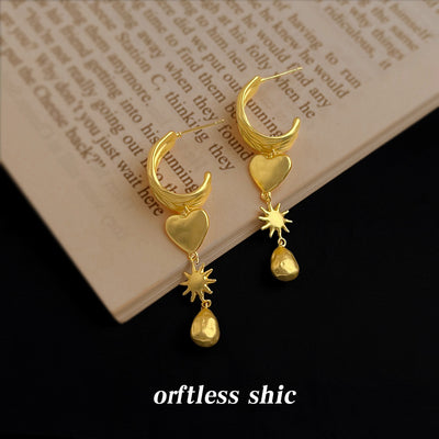 Matte gold heart starburst teardrop earrings on open book pages