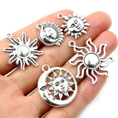 Overview of silver-tone celestial charms combining sculpted sun faces, rays and crescent moons arranged on a light backg