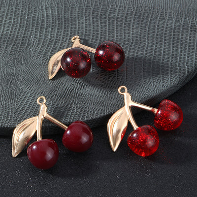 Three cherry charms with pairs of red resin cherries and gold-tone leaves on a grey and black background