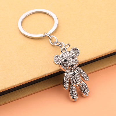 Clear rhinestone bear charm hanging from a silver-tone key ring beside a yellow book.