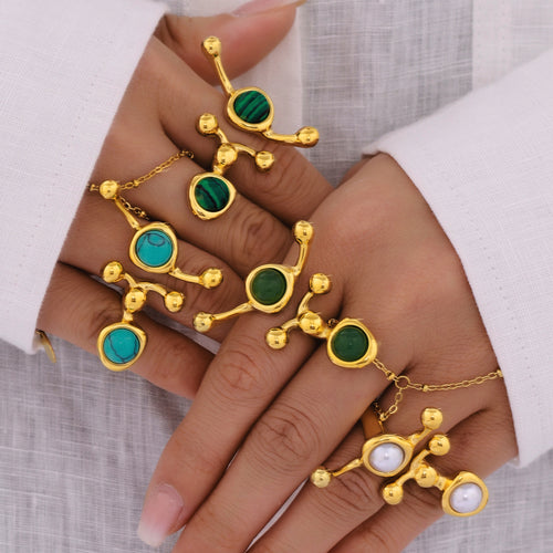 Hands wearing multiple abstract dual stone open rings in gold tones