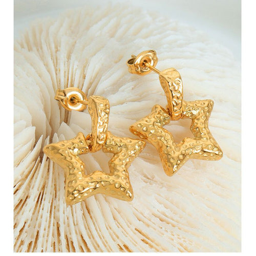 Pair of gold hammered open star drop earrings on white coral surface