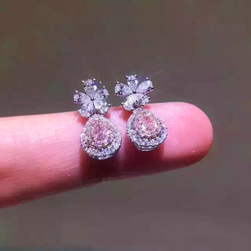 Front view of pink teardrop double-halo drops with flower tops on finger