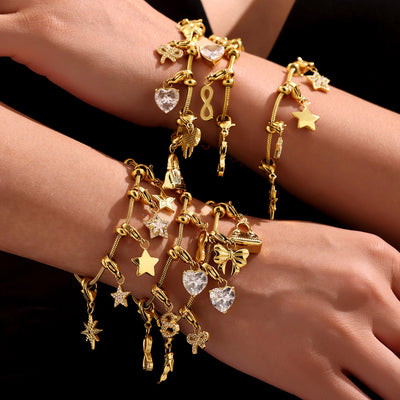 Stacked gold charm bracelets on wrists with hearts stars bows