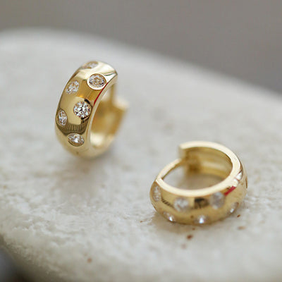 Gold CZ thick huggie hoops resting on white stone surface