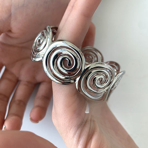 Close-up of silver spiral disc open cuff bracelet held in hands