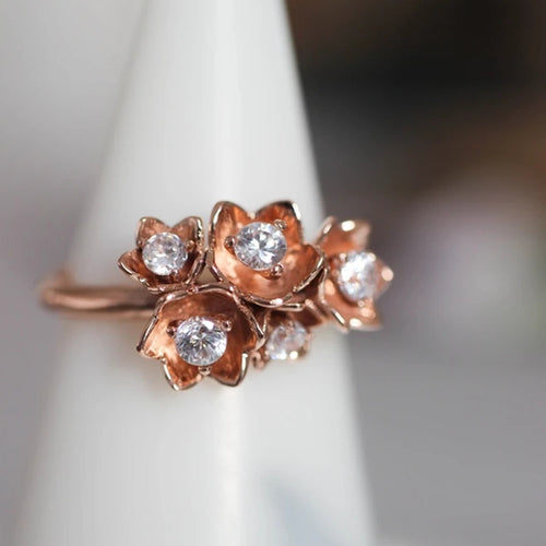 Close-up rose gold multi-flower CZ cluster ring on white stand