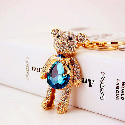 Angled front view of a rhinestone bear keychain beside a white printed box.