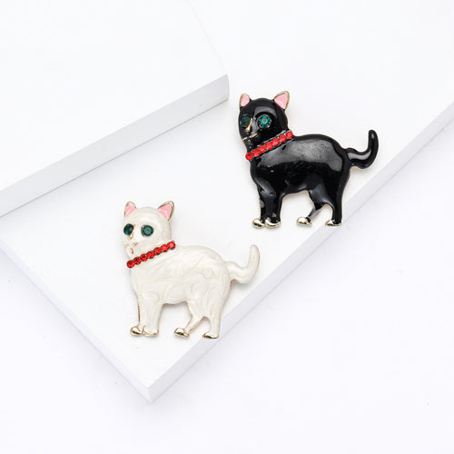 White and black enamel cat brooches displayed together on white blocks